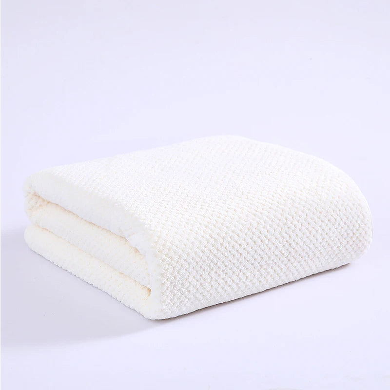 A stack of white plush coral velvet bath towels folded neatly on a white surface.