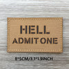 A rectangular tan woven patch with black text spelling out HELL ADMIT ONE on a weathered wooden surface.