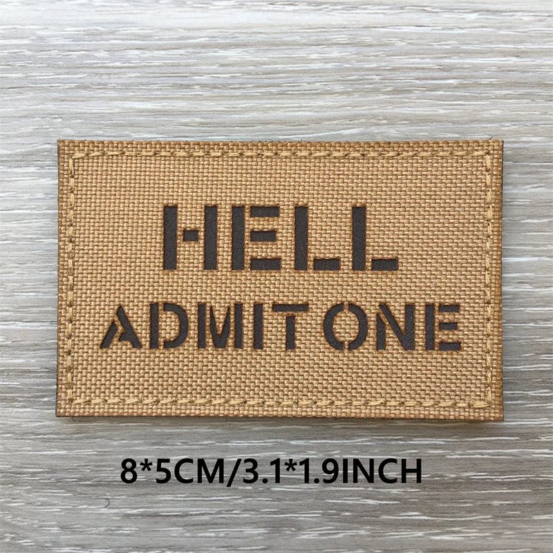 A rectangular tan woven patch with black text spelling out HELL ADMIT ONE on a weathered wooden surface.