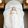 A white bed with a mosquito net draped over it, featuring a blue trim and a person lying in the center.
