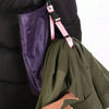 A close-up of a pink luggage strap with an ID tag attached to a dark green fabric item.