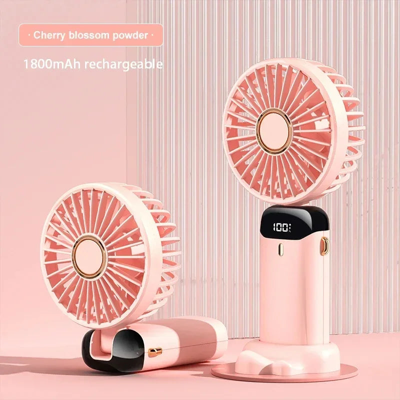 A pink foldable neck fan with an LED display and phone stand is shown on a light pink surface.