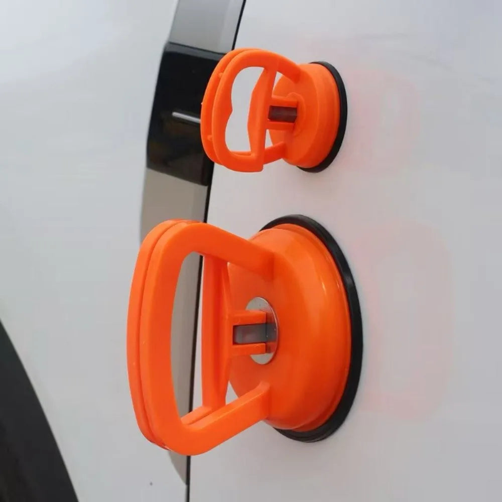 Orange heavy-duty suction cup dent puller tool mounted on a white surface.