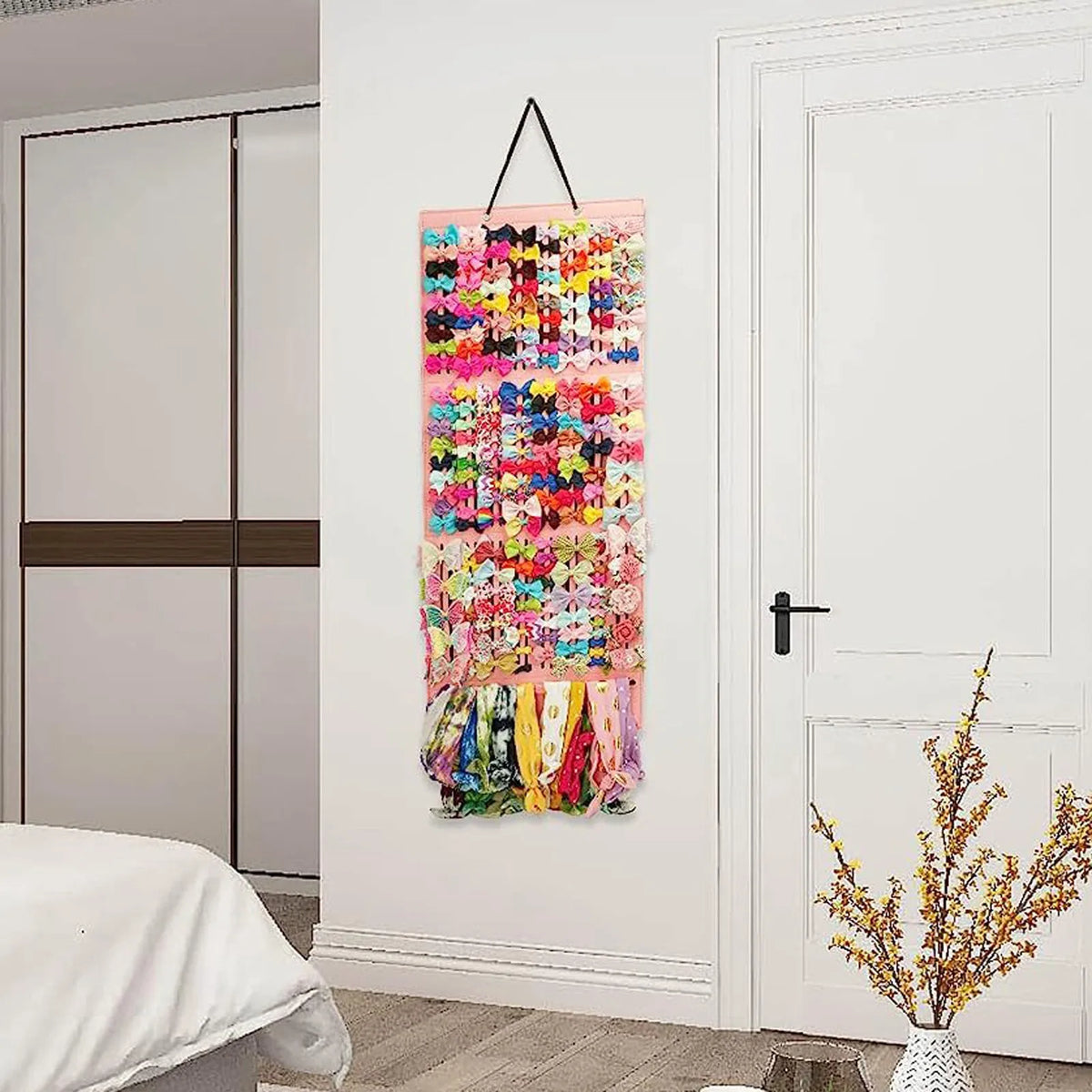 A colorful hair bow and clip organizer with a rope hanger displayed on a white wall.