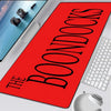 A red oversized gaming mouse pad with the title BOONDOCKS printed in black text is shown next to a white keyboard.
