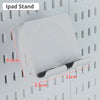 A white iPad stand is mounted on a pegboard organizer with hooks and shelves.