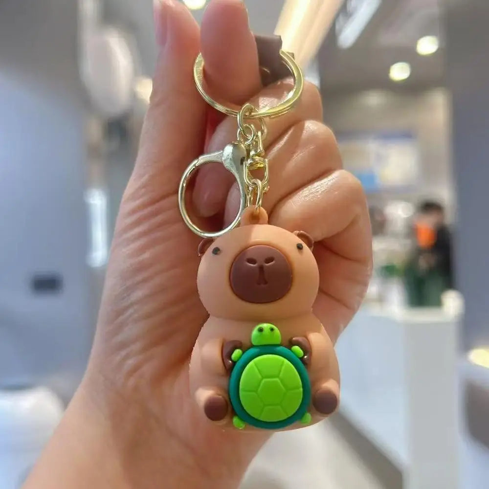 A hand holds an adorable capybara keychain charm with a green turtle accessory.