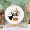 A circular embroidery hoop displaying a floral arrangement and a black cat design on white fabric.