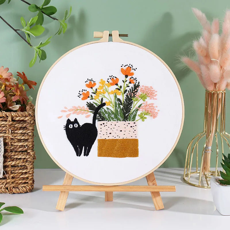 A circular embroidery hoop displaying a floral arrangement and a black cat design on white fabric.
