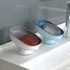 A set of blue and gray suction cup soap holders with drainage trays sitting on a white countertop.