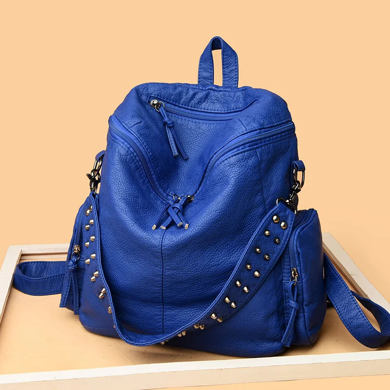 A deep blue soft leather backpack featuring silver rivets and a drawstring closure.