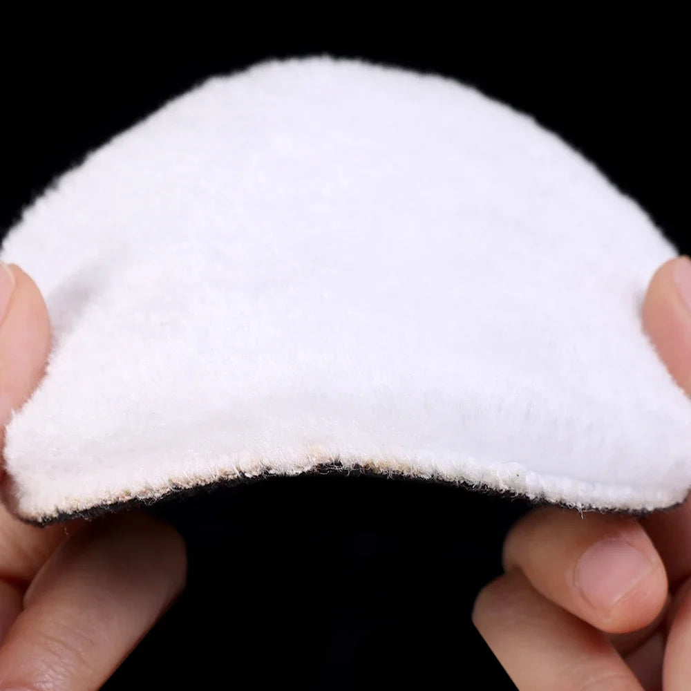 A white car polishing pad set with wool discs held between fingers against a black background.