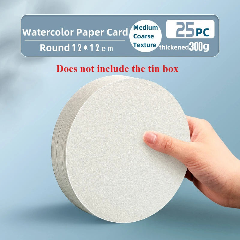 A hand holds a round piece of white watercolor paper card with a coarse texture.