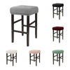 A set of four bar stools with gray, maroon, and green fabric slipcovers.