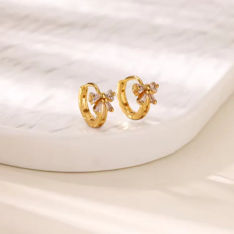 Pendientes de aro dorados con acentos florales de circonita cúbica sobre una superficie de mármol blanco.