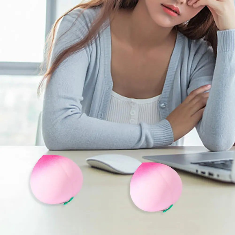 Deux jouets anti-stress en forme de pêche roses posés sur un bureau à côté d'un ordinateur portable.