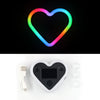 A glowing heart-shaped LED light ring in a rainbow gradient, next to a black heart-shaped device and some clear lenses.