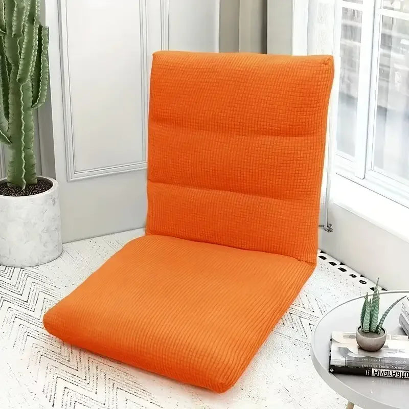 An orange foldable floor sofa cover for a single seat is displayed next to a potted cactus by a window.