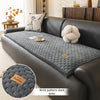 A dark gray quilted fabric sofa cover with a textured pattern displayed on a modern leather sofa.