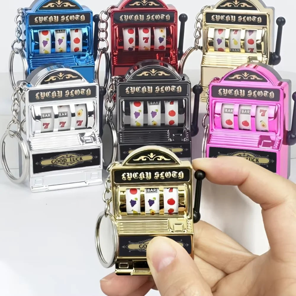 A hand holds a gold mini fruit slot machine keychain fidget toy with colorful fruit symbols.