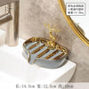 A gold leaf-shaped ceramic soap dish with a drain rack is placed on a white bathroom counter.