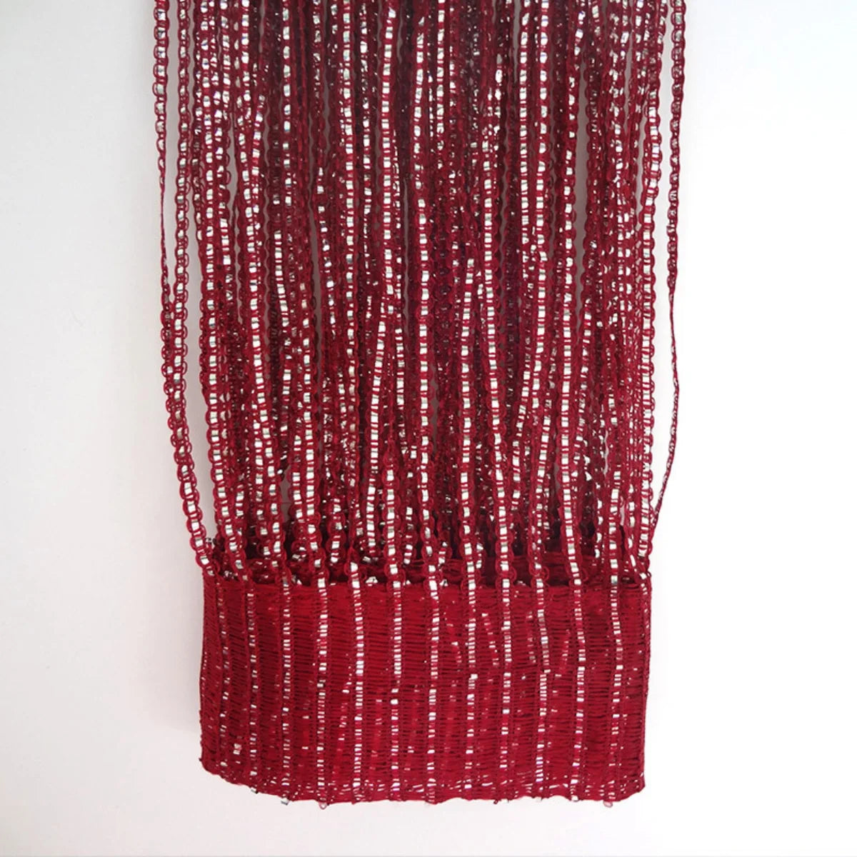 A vertical curtain made of deep red woven tassels hanging against a white background.