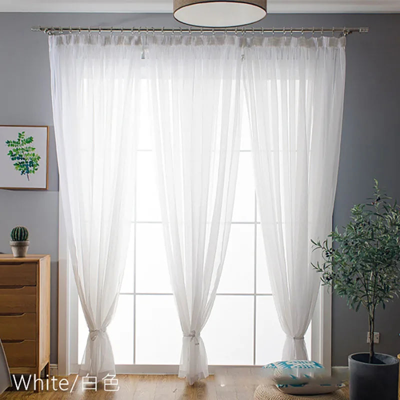 White sheer voile curtains with rod pockets hanging in front of a large window.