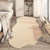A beige irregular area rug with a plush soft texture placed on a light wood floor next to a bed and white decor.