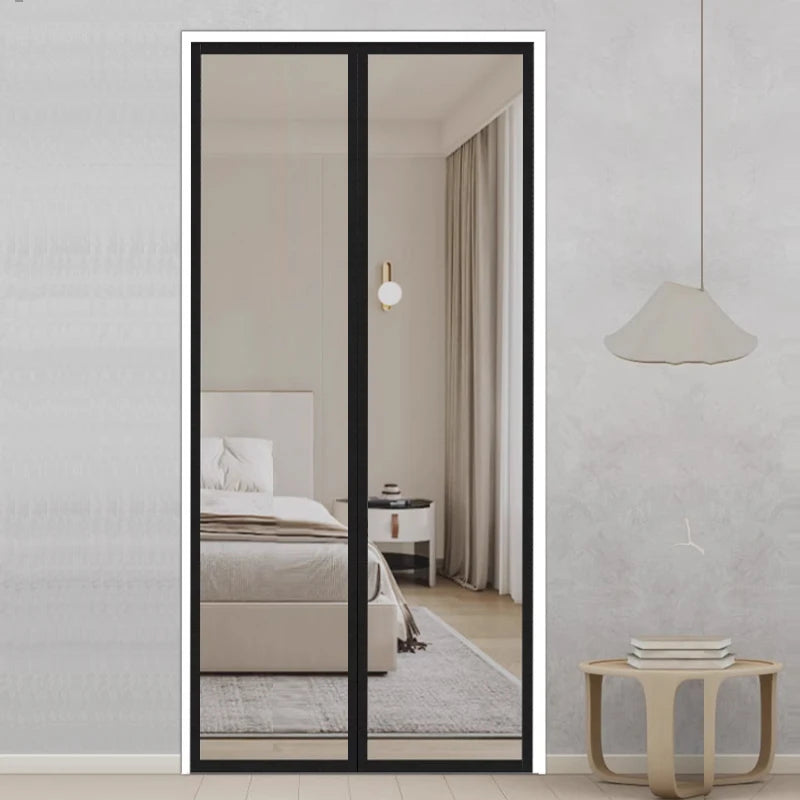 A full-length mirror framed in black, reflecting a bedroom interior with white bedding and light gray curtains.