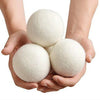 A pair of hands holds a set of three white natural wool dryer balls.