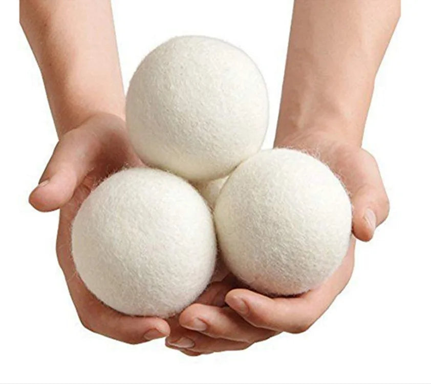 A pair of hands holds a set of three white natural wool dryer balls.