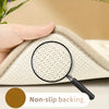 A hand holds a beige plush velvet bathroom mat with non-slip backing, magnified by a black lens.