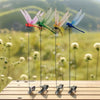 Five lifelike dragonfly garden clips with insect repellent designs hanging from thin wires on a wooden surface.
