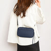 A woman wearing a white jacket is holding a navy blue passport and document organizer wallet.