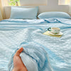 A hand is touching a light blue waffle-weave quilt on a bed with white pillows.
