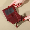 A close-up of a maroon PU leather wallet with a flap and zipper is held by a hand against a beige background.