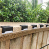 A row of black solar-powered LED step lights mounted on a textured stone wall outdoors.