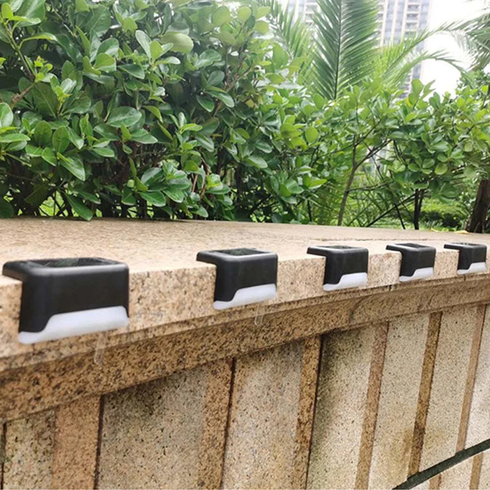 A row of black solar-powered LED step lights mounted on a textured stone wall outdoors.