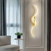 A modern minimalist LED wall lamp with a curved, glowing yellow light fixture mounted on a white wall.