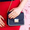 A dark blue clutch bag with silver metal pyramid studs and four prongs resting on a red fabric.