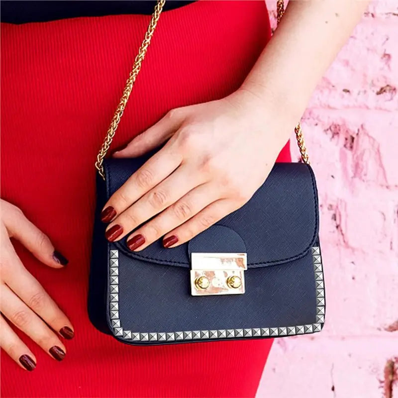 A dark blue clutch bag with silver metal pyramid studs and four prongs resting on a red fabric.