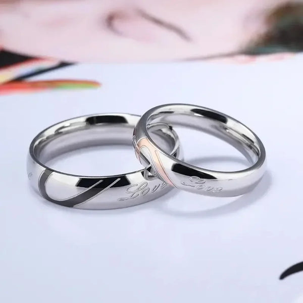 Two silver stainless steel promise rings for couples lying on a white surface.