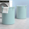 A light blue and white striped foldable laundry basket with handles sitting on a light gray floor.