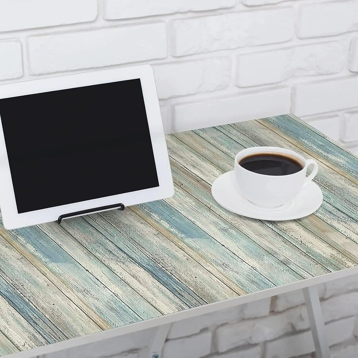 A white tablet rests on a light blue distressed wood grain table next to a white cup of coffee.