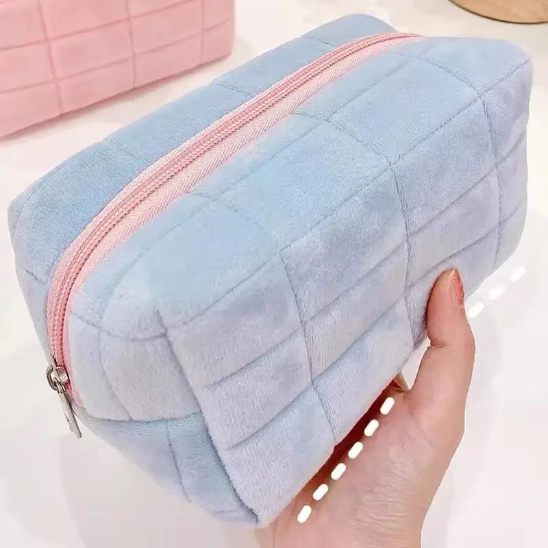 A light blue suede portable makeup bag with a pink zipper is held in a hand.