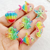 Hand holding colorful resin charms shaped like fish, starfish, and sea creatures for crafting