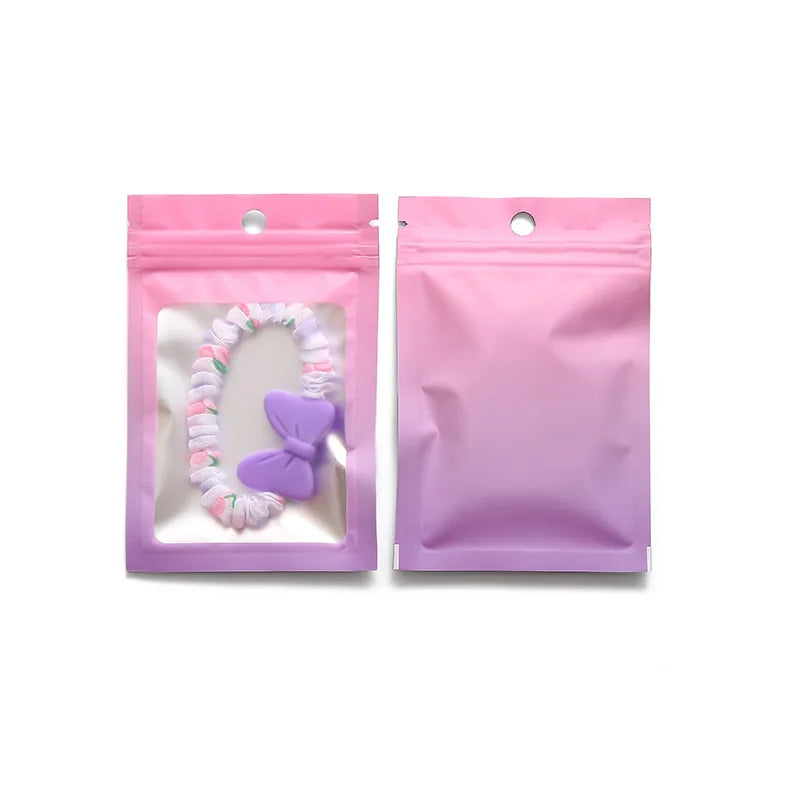 A pair of pink gradient resealable zipper pouches with clear windows, one containing a purple beaded item.