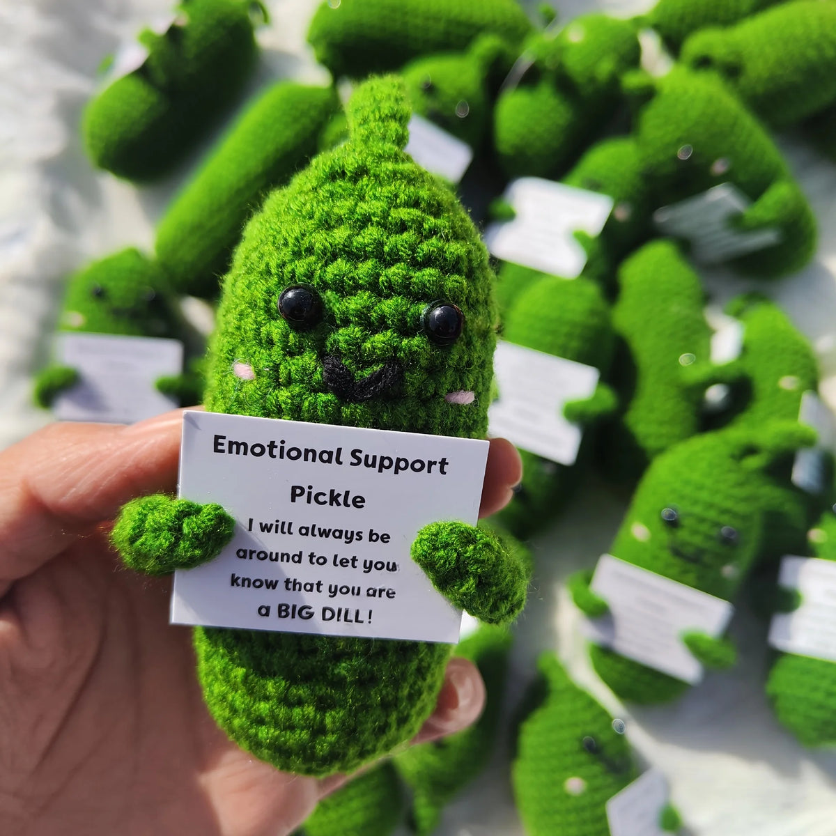 Handcrafted pickle plush with a muppet face surrounded by other green stuffed items.