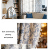 A close-up of a light blue and white floral cotton-linen curtain with tasseled edges.