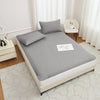 A gray waterproof mattress protector is displayed on a bed, featuring elastic straps and a quilted surface.